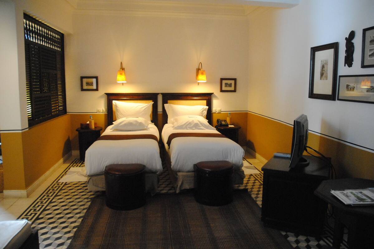 A hotel room with two beds, bedside tables, a television, and a patterned rug.