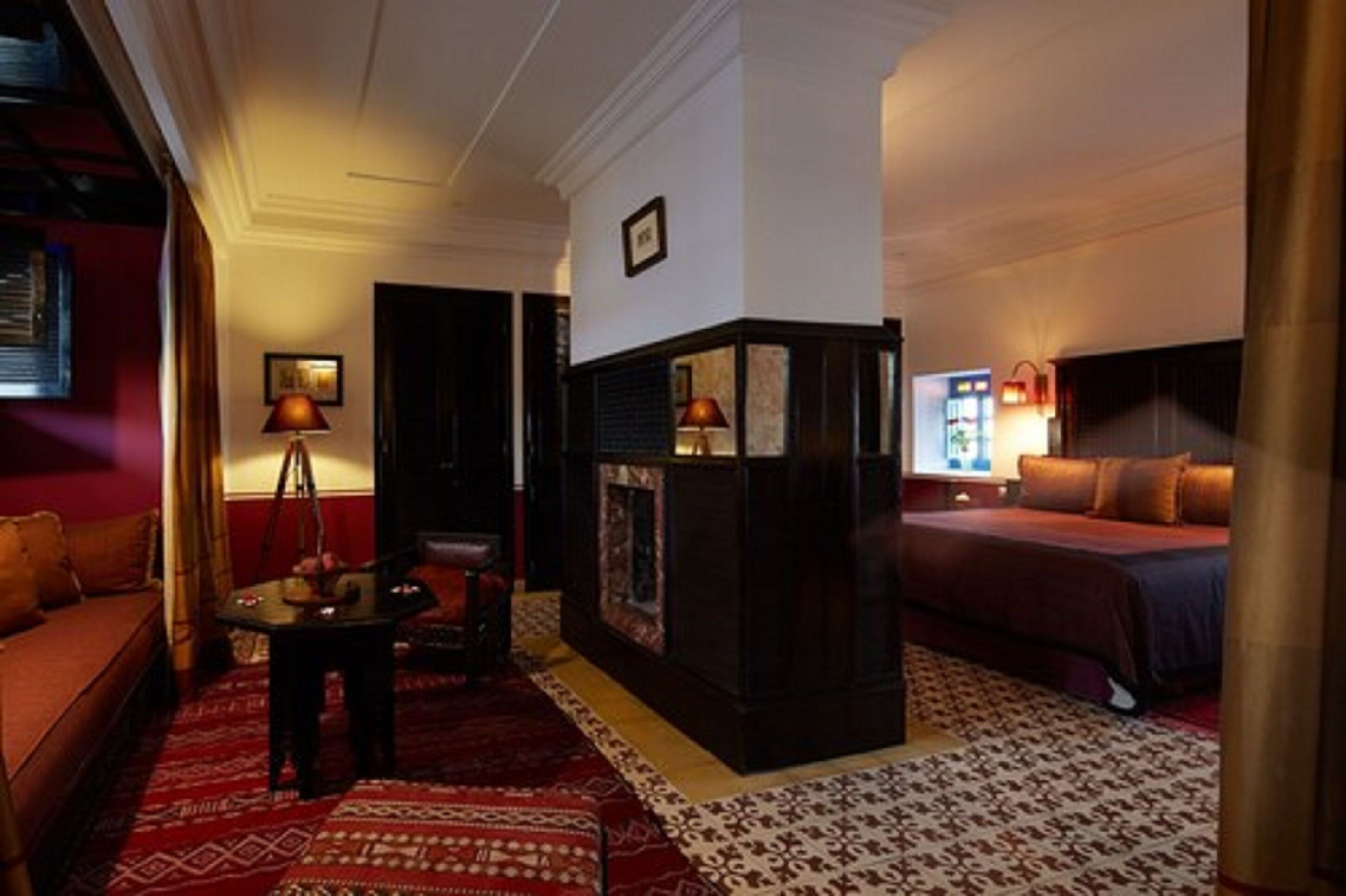 Une chambre d’hôtel avec un canapé rouge, une petite table, une cheminée et un lit recouvert d’une couverture rouge.
