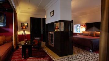 Une chambre d’hôtel avec un canapé rouge, une petite table, une cheminée et un lit recouvert d’une couverture rouge.
