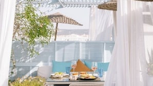 An outdoor dining area with a table set for two, featuring a blue cushion, wine glasses, and plates of food. - Heure Bleue Palais (Essaouira)
