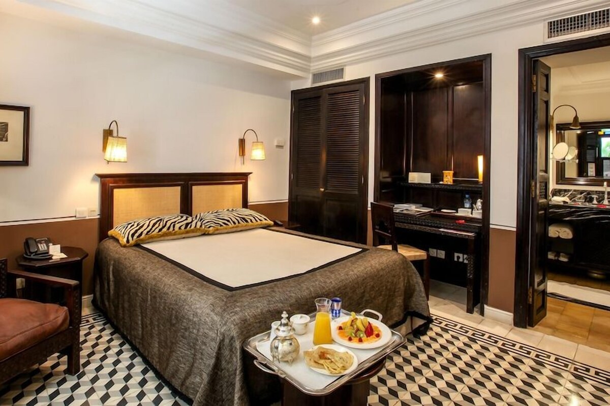 A hotel room with a bed, bedside table, chair, desk, and a tray with breakfast items.