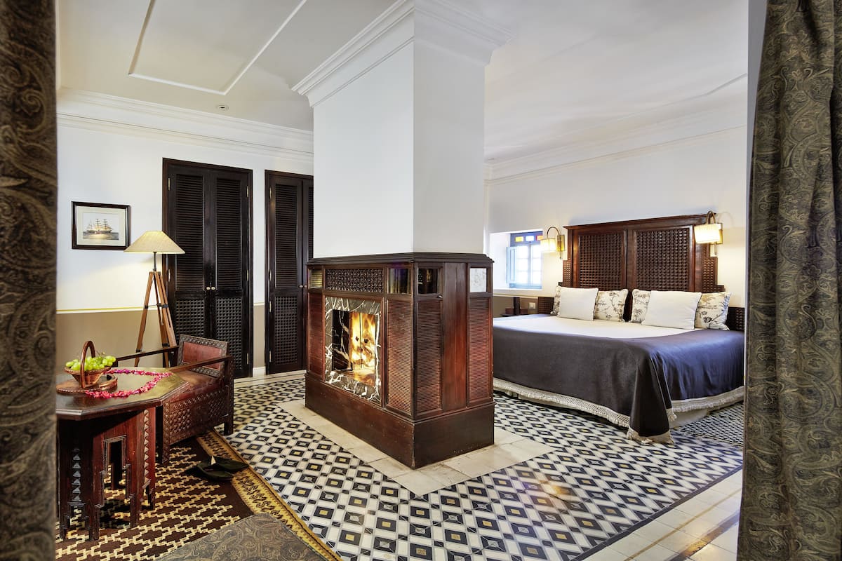 A hotel room with a bed, a fireplace, a desk with a lamp, and a patterned floor.