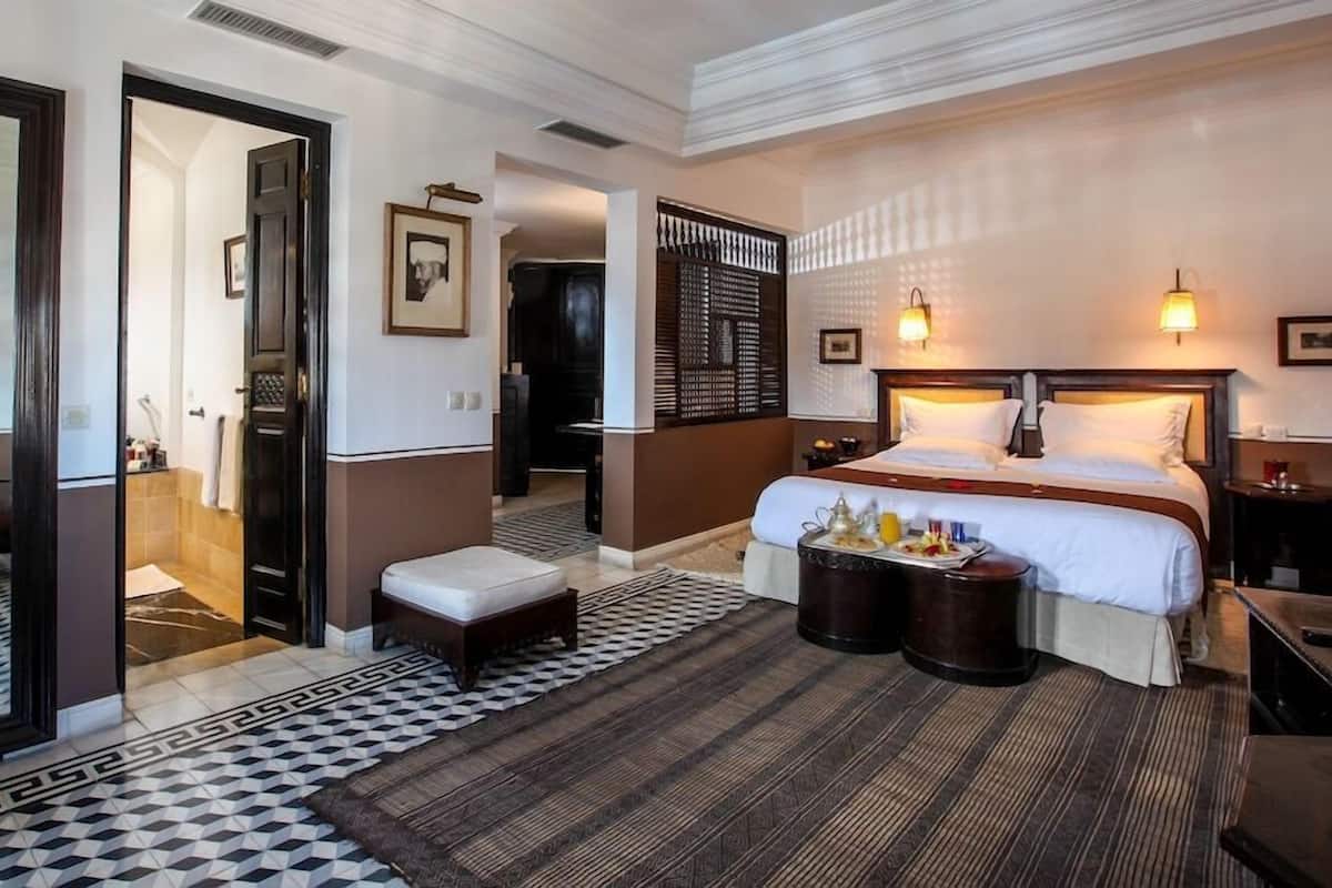 A hotel room with a large bed, bedside tables, a mirror, a patterned rug, and a view of the hallway.