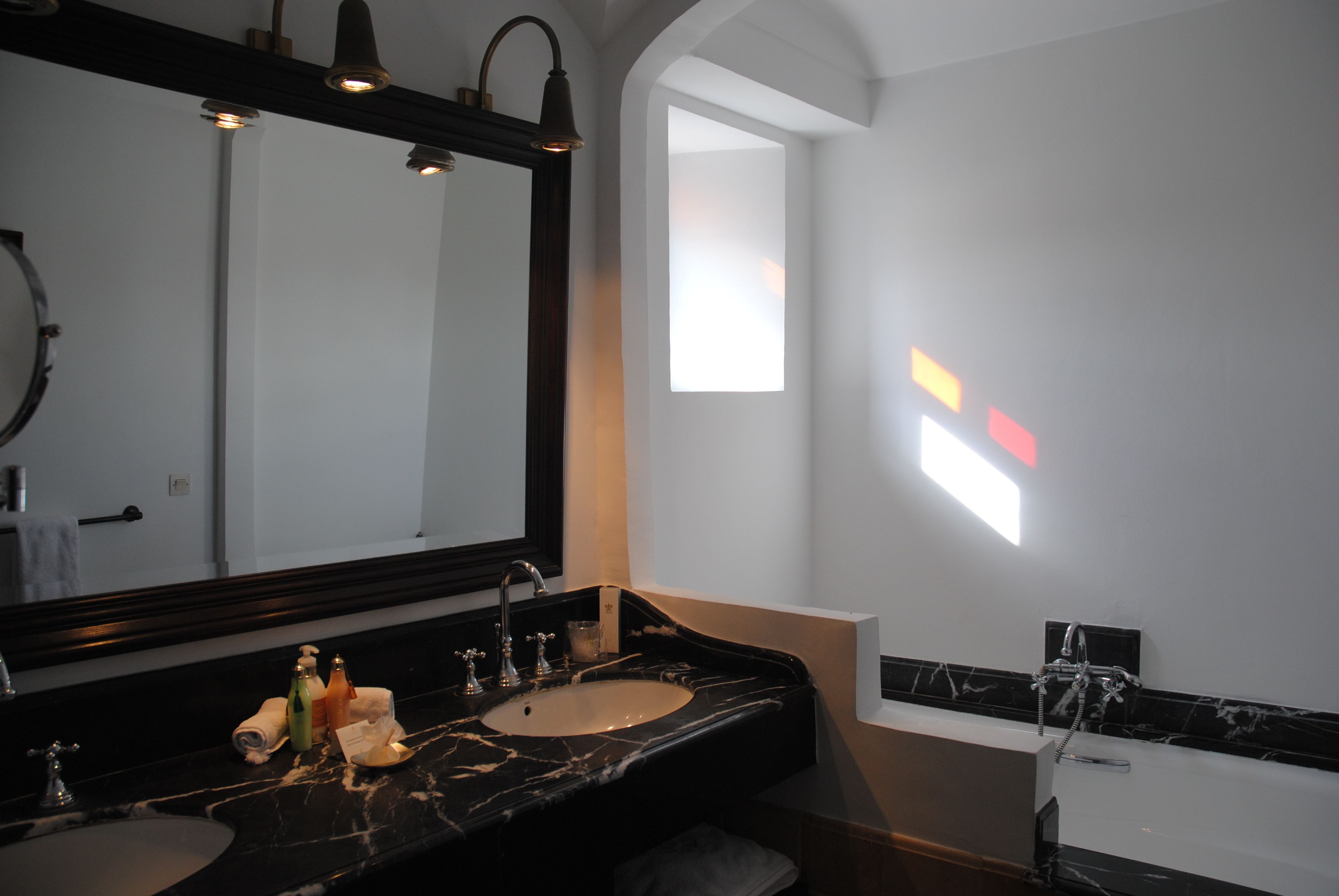 A modern bathroom with a large mirror, two sinks, a bathtub, and a window providing natural light.