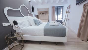 A modern bedroom with a white bed, a geometric side table, a wall-mounted TV, and a window with curtains.