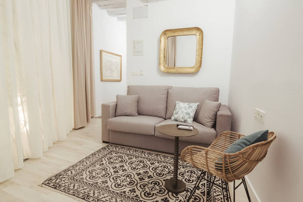 A living room with a sofa, a round coffee table, a wicker chair, a patterned rug, and a mirror on the wall.