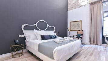A modern bedroom with a white bed, grey bedding, a geometric side table, and a desk with a chair.