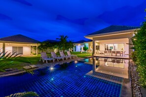 A modern hotel with a swimming pool, lounge chairs, and a well-lit patio area. - Hua Hin Pool Villa with 4 Bedrooms L50 (Hua Hin)