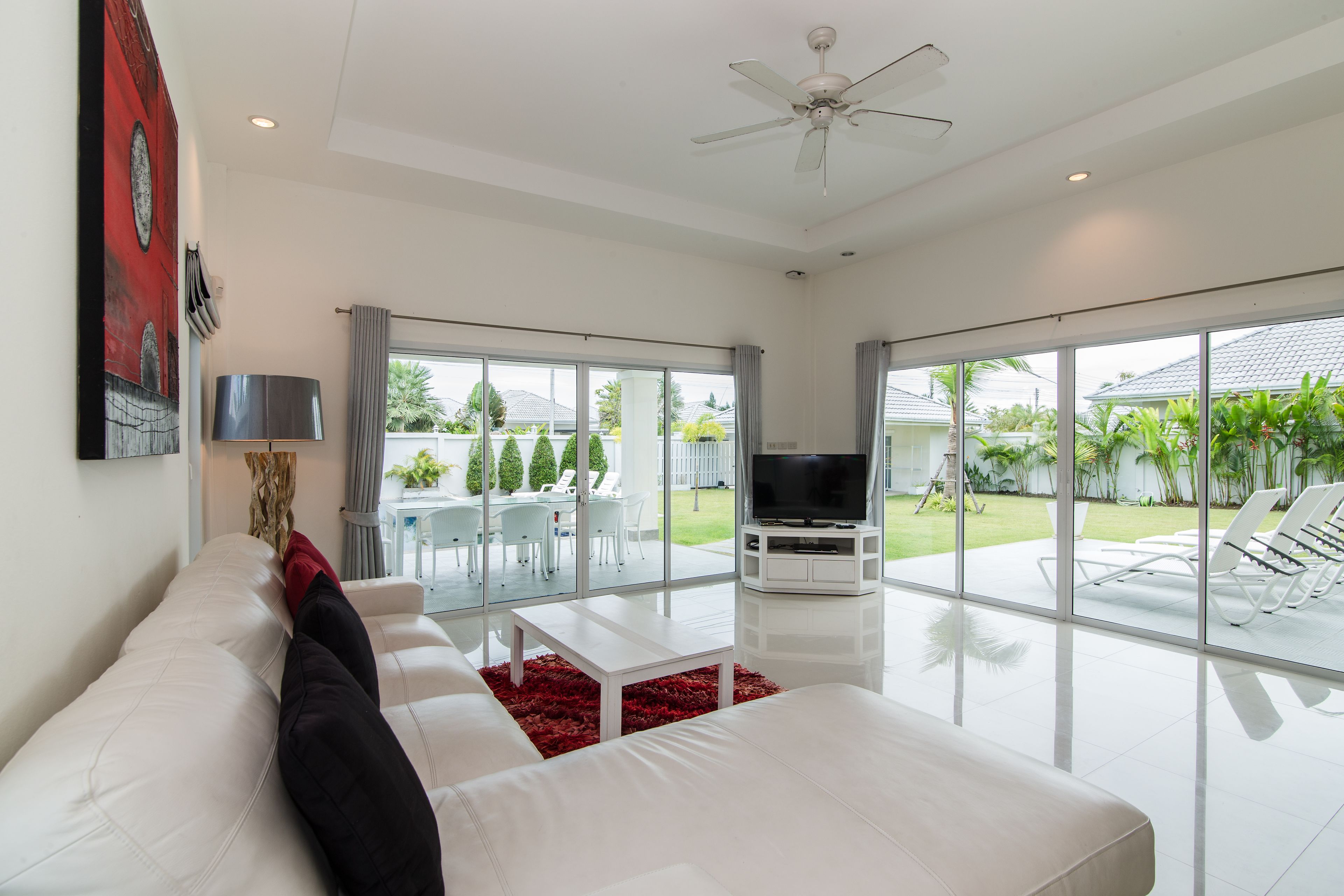 A modern living room with a white sofa, a red rug, and a flat-screen TV.