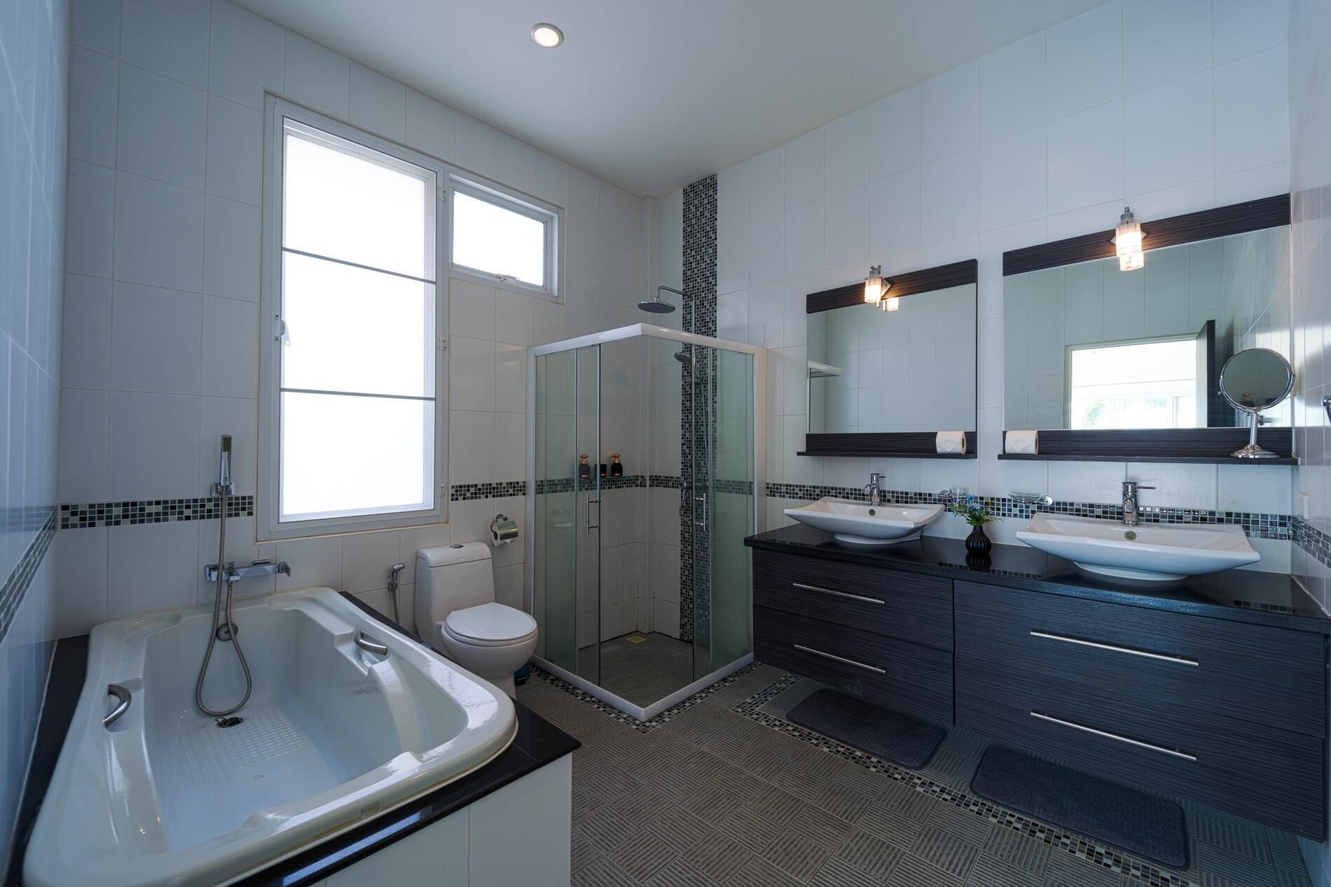 A modern bathroom with a bathtub, two sinks, a toilet, and a glass-enclosed shower.