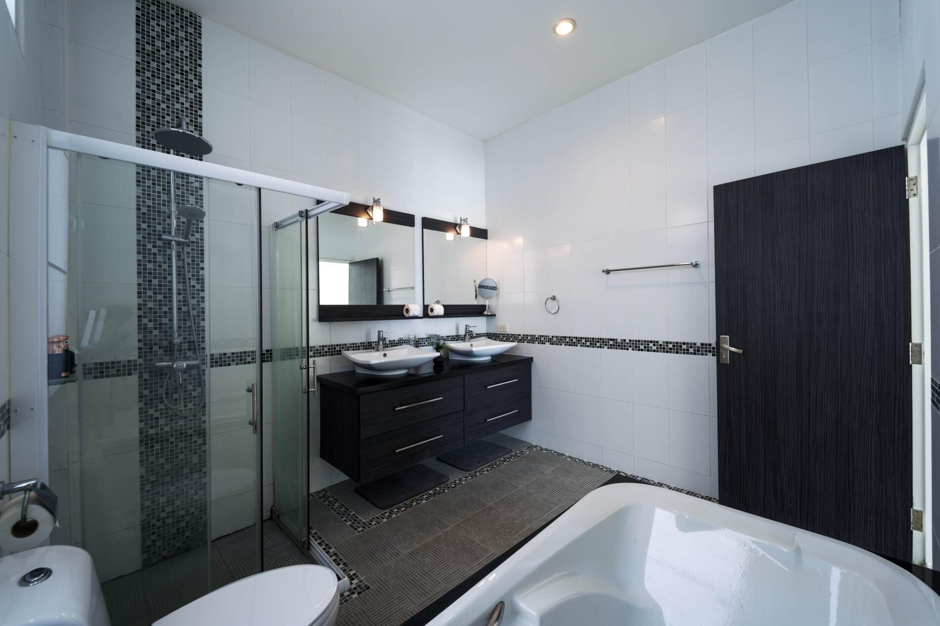 A modern bathroom with a glass-enclosed shower, two sinks, a large mirror, and a dark wood door.