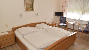 A bedroom with a wooden bed, a desk, a chair, a TV, and a window with curtains.