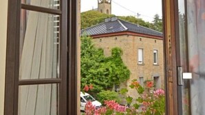 An open window with a view of a building with a tower, a car parked outside, and a flower box with pink flowers. - Weinhaus Hehner Kiltz (Waldböckelheim)