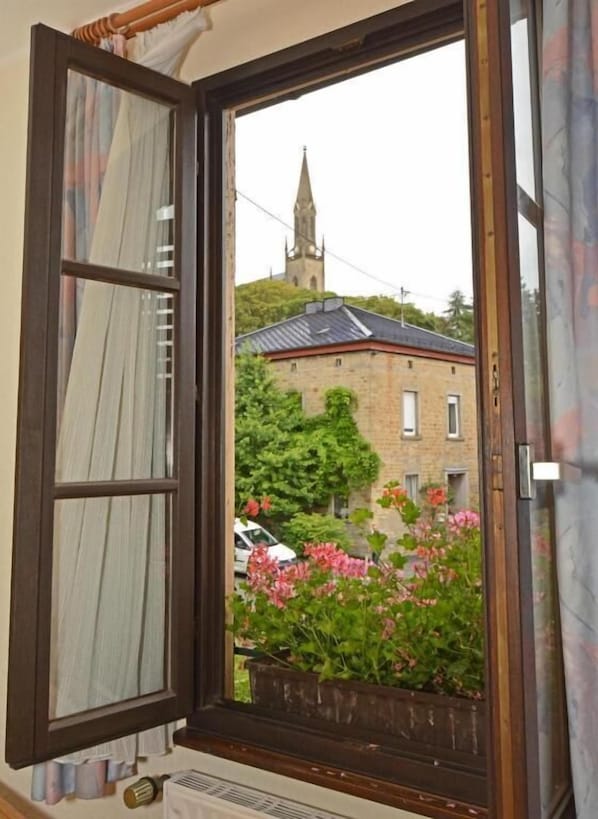 An open window with a view of a building with a tower, a car parked outside, and a flower box with pink flowers. - Weinhaus Hehner Kiltz (Waldböckelheim)