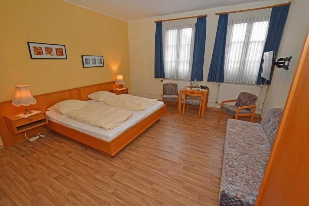 A hotel room with a bed, two chairs, a small table, a sofa, and a TV.