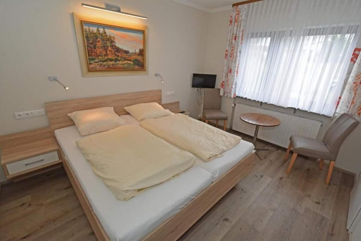 A bedroom with a bed, a TV, a chair, and a painting on the wall.