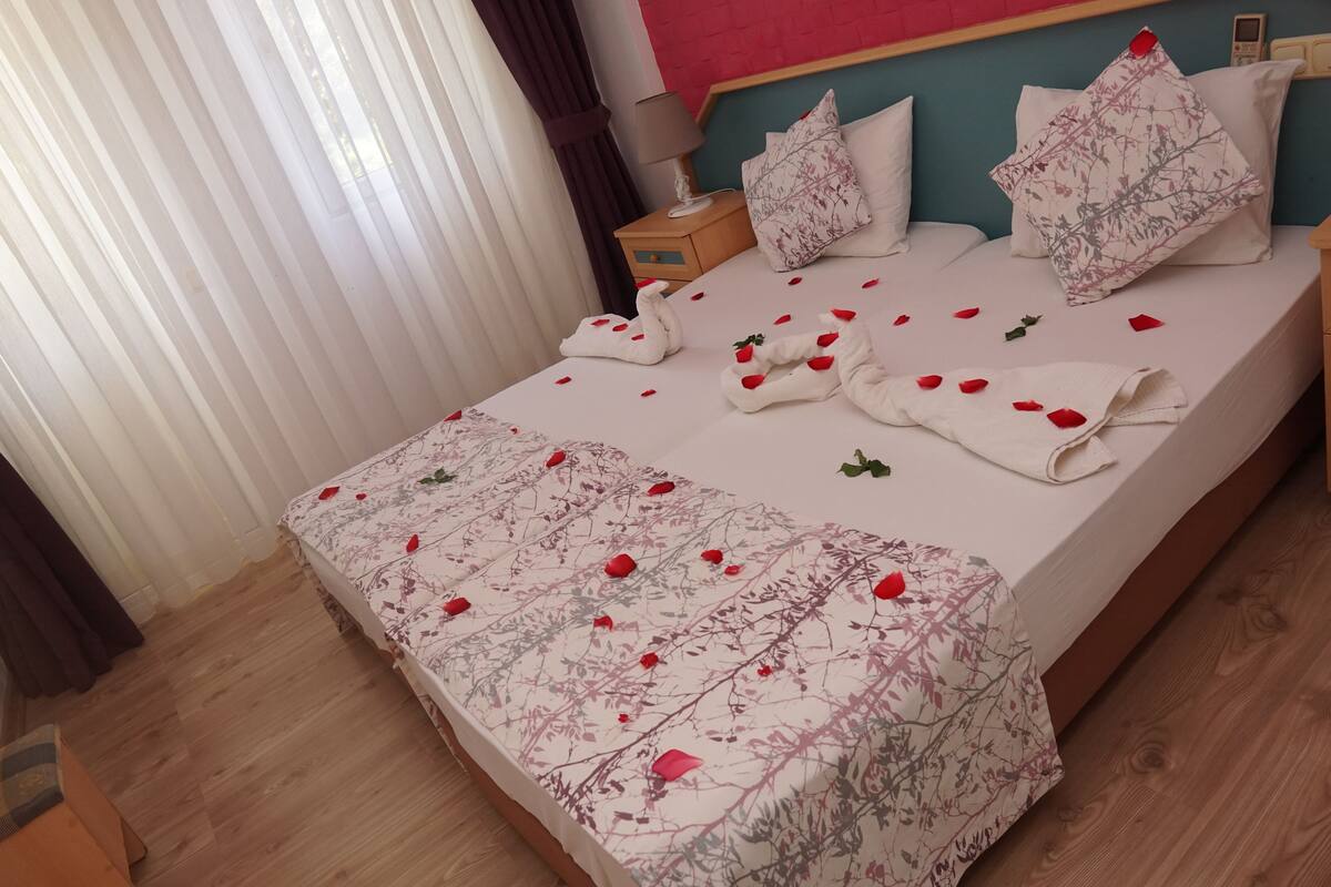 Cama bem arrumada com roupa de cama florida, mesa de cabeceira com abajur e cabeceira com almofadas decorativas.