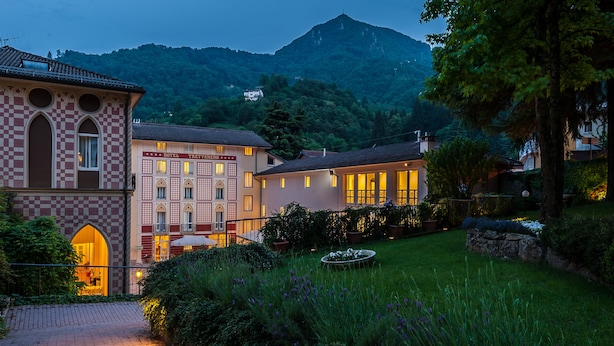 Um hotel com fachada quadriculada, um jardim bem cuidado e montanhas ao fundo.