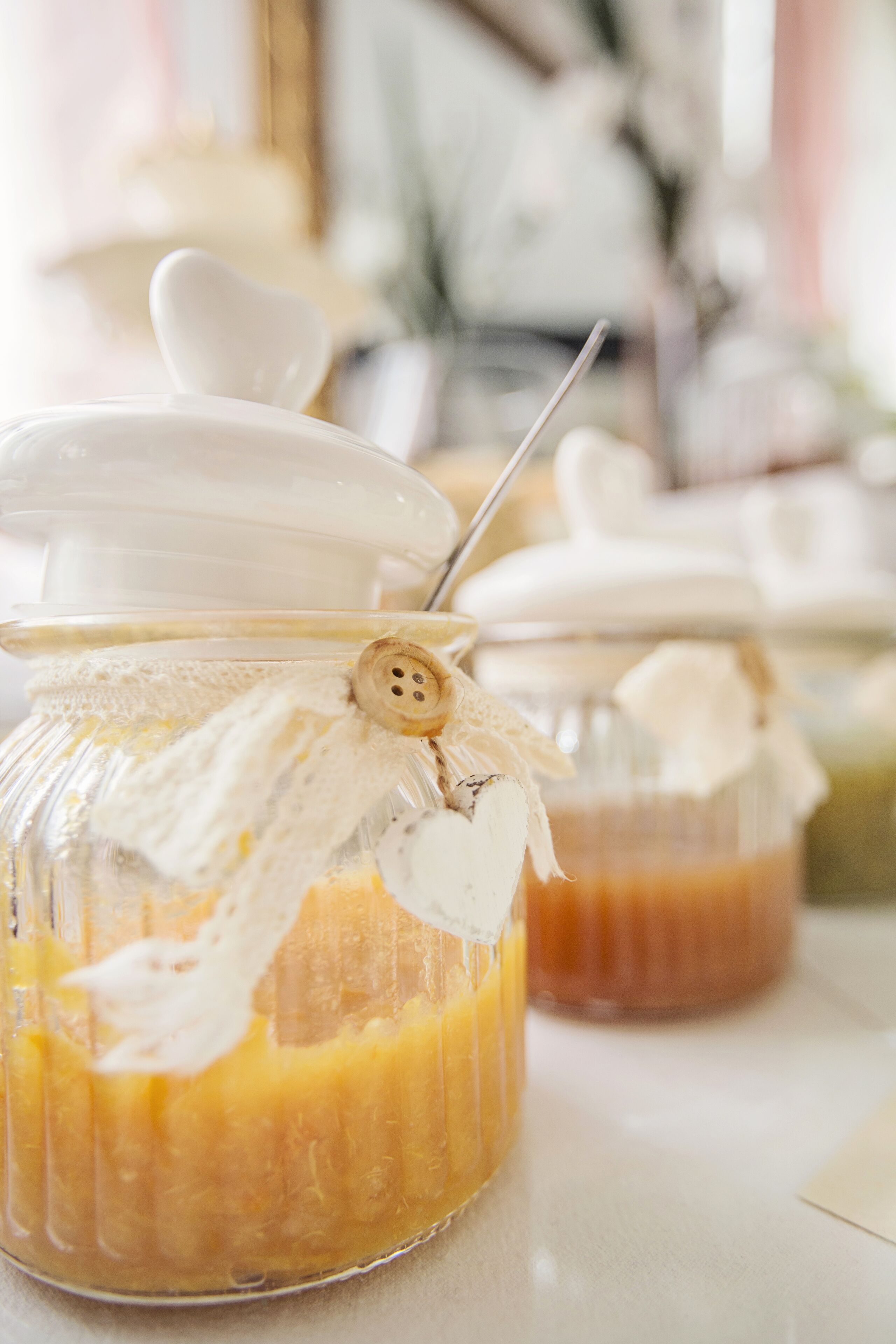 Two glass jars with white lids, one with a button and a white ribbon, containing a yellowish substance.
