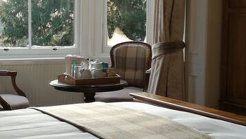 A hotel room with a bed, a chair, a small table with toiletries, and a window with a view of trees.
