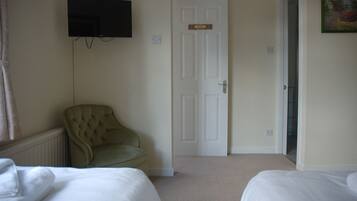 A hotel room with two beds, a television mounted on the wall, a door with a nameplate, and a painting on the wall.