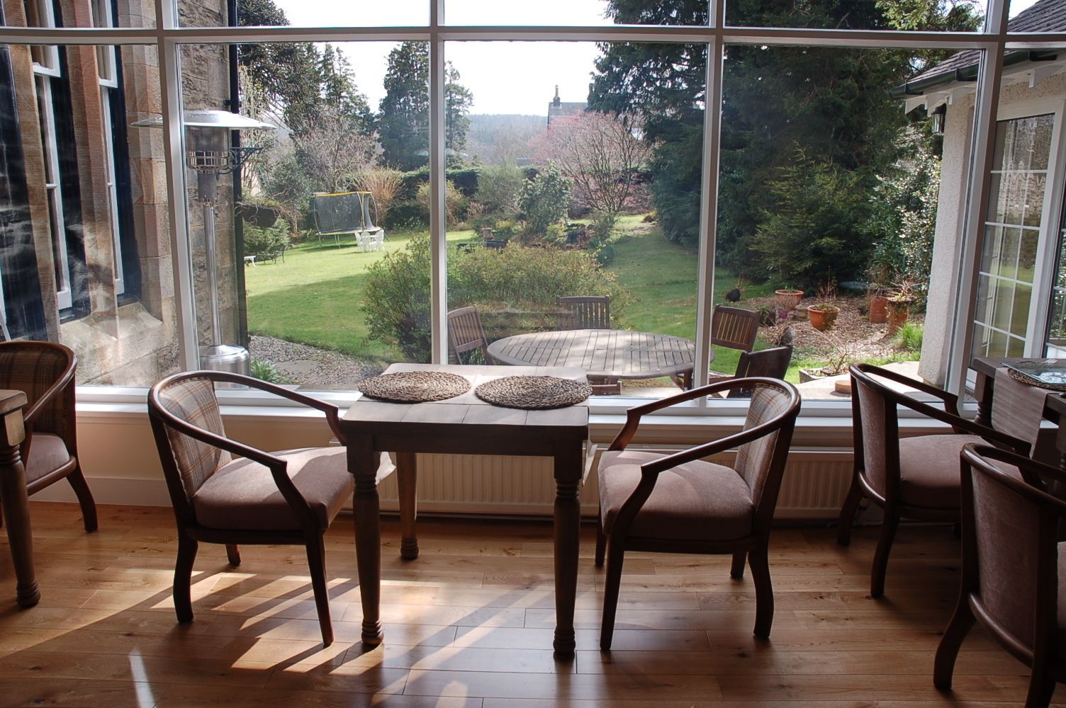 Ein Essbereich mit Tisch und Stühlen, große Fenster mit Blick auf einen Garten und Bäume.