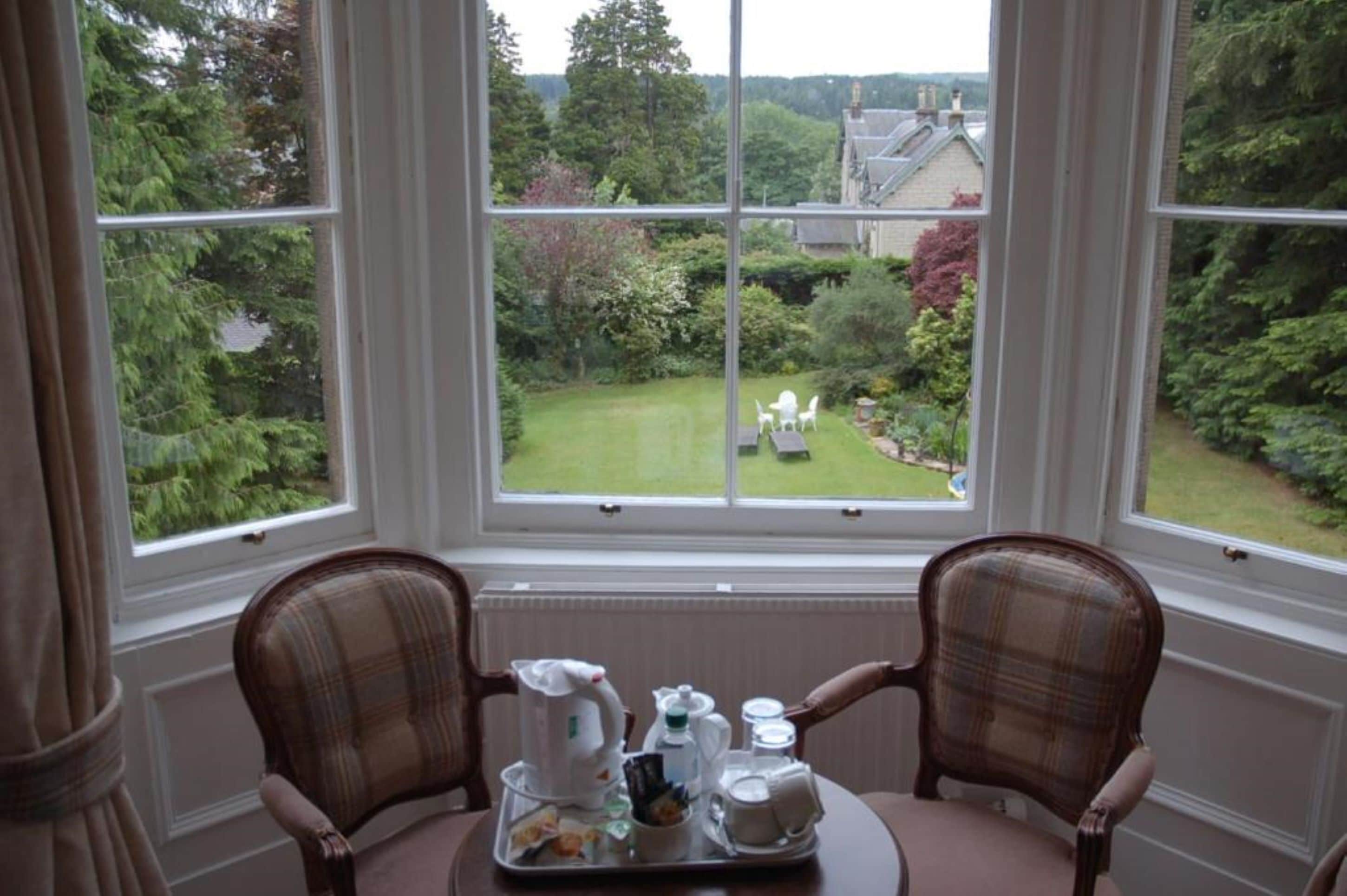 Habitación con un amplio ventanal que da a un jardín. Hay una mesa con una bandeja de alimentos para el desayuno.