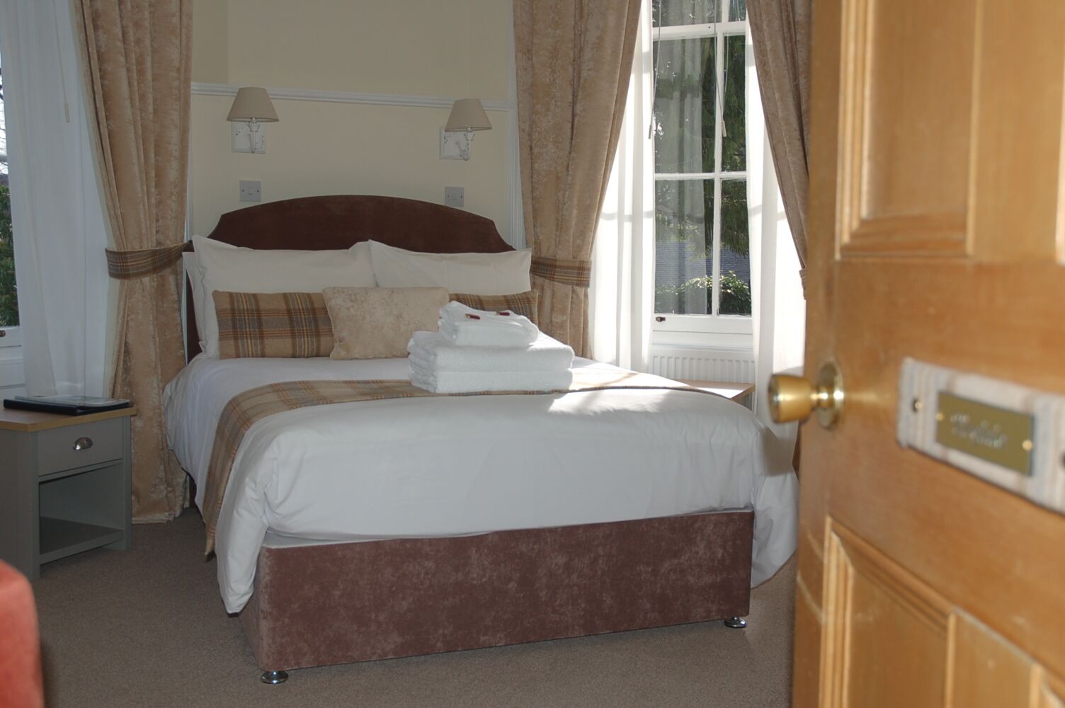 A hotel bedroom with a bed, a nightstand, a lamp, and a window with curtains.