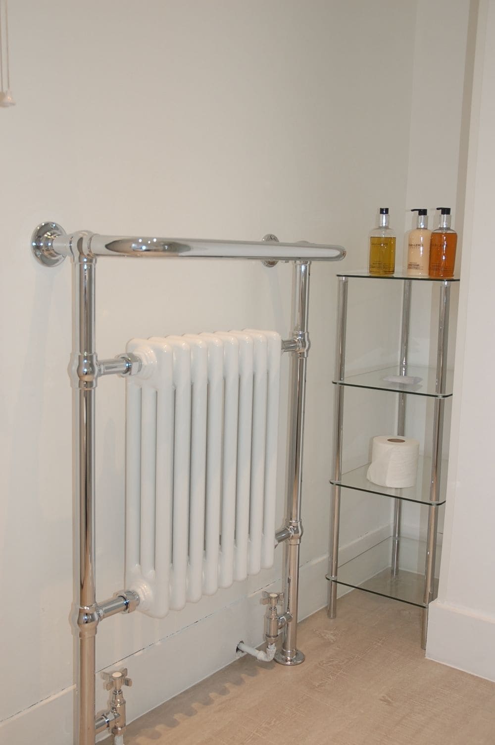 A bathroom with a glass shower enclosure, a white radiator, and a glass shelf with toiletries.