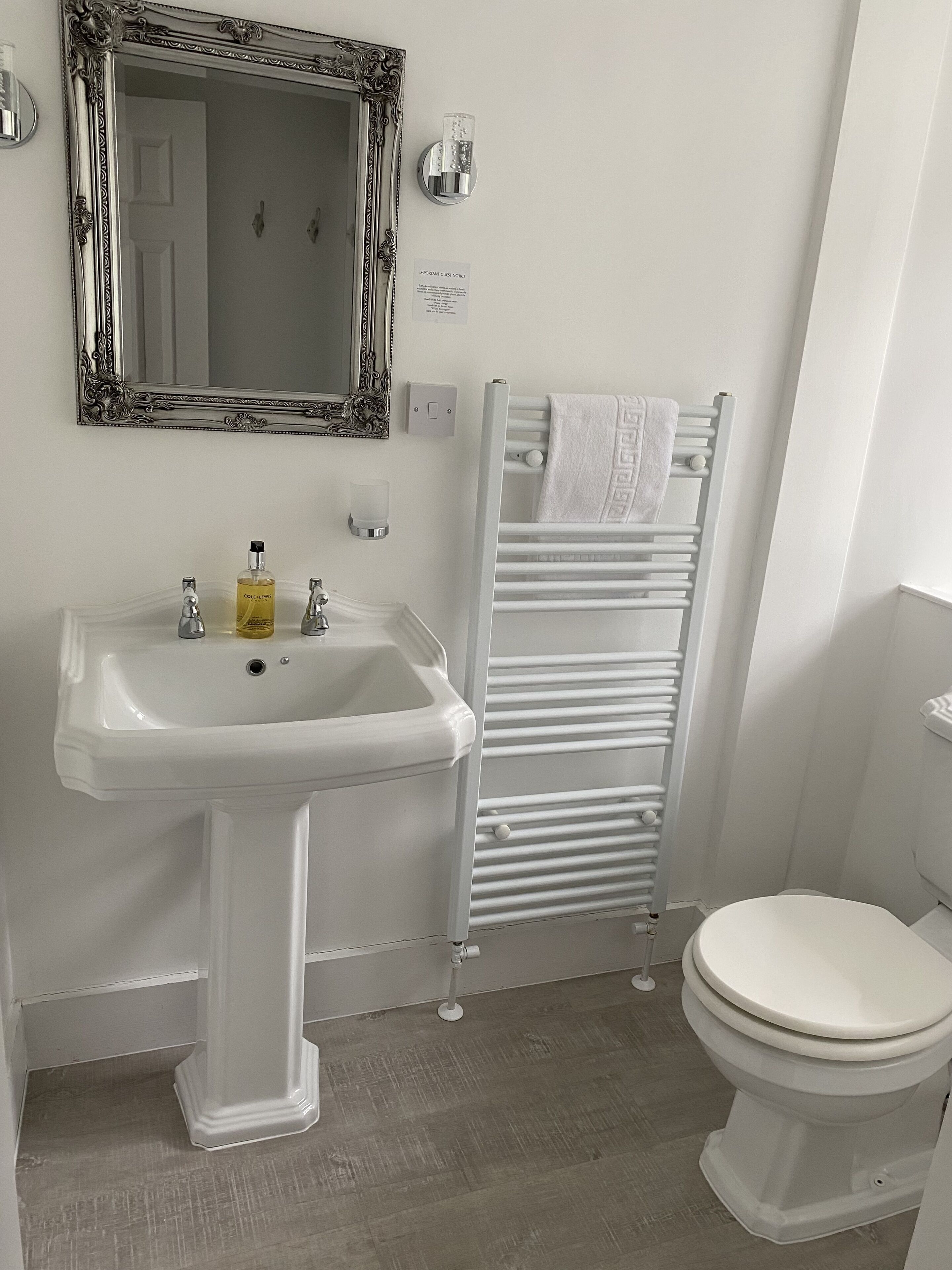 Ein Badezimmer mit einem Standwaschbecken, einem Spiegel, einem Handtuchhalter und einer Toilette.