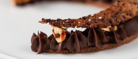 A chocolate tart with a flaky crust and a glossy chocolate ganache filling, garnished with nuts.