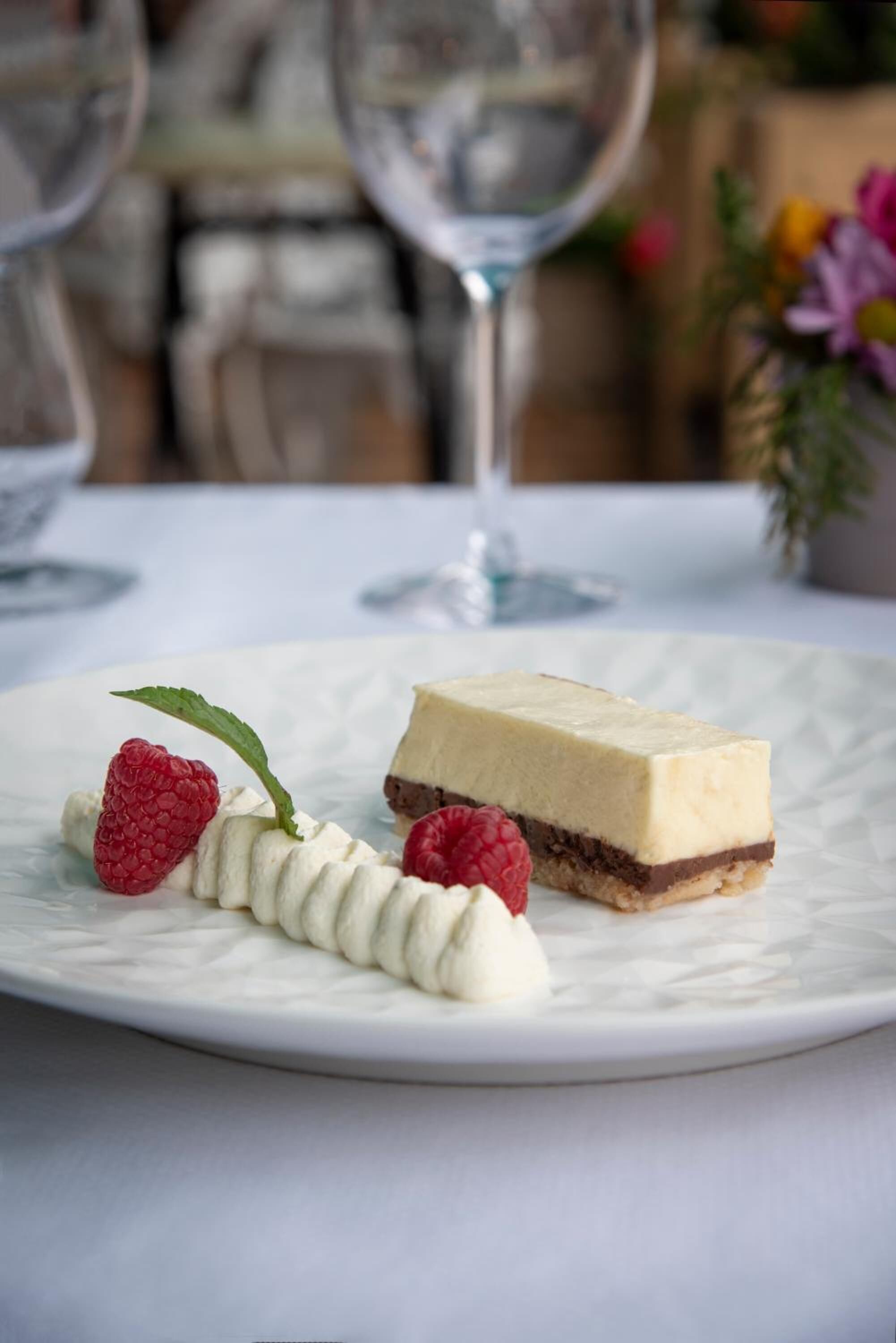 Une assiette de dessert avec un morceau de gâteau au fromage et des framboises, le tout présenté sur une assiette blanche.