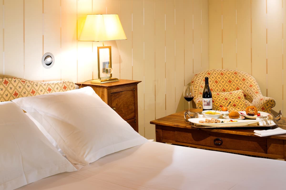 A hotel room with a bed, a nightstand with a lamp, a chair, and a tray with breakfast items.