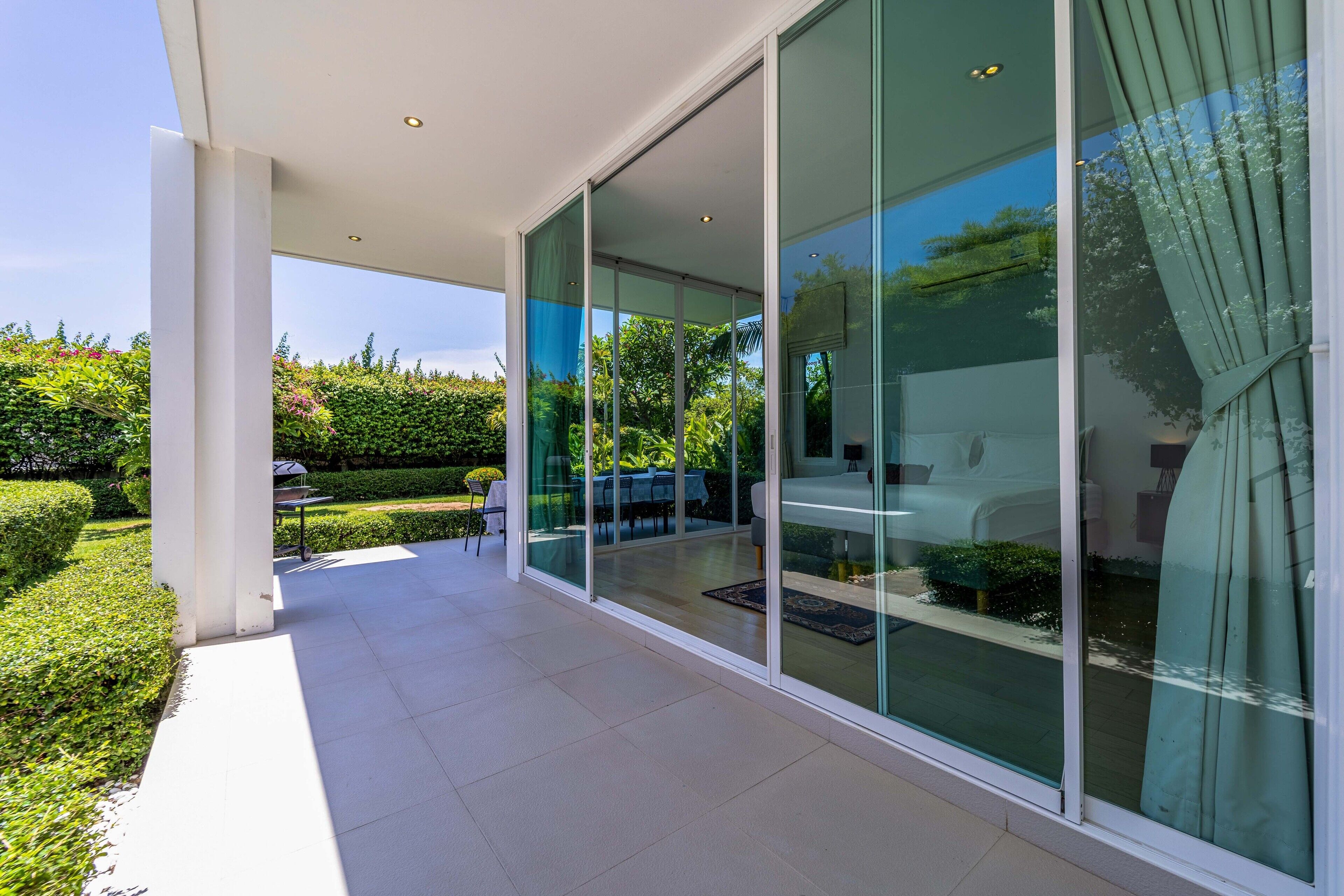 A modern outdoor patio with glass doors leading to a seating area, surrounded by greenery.