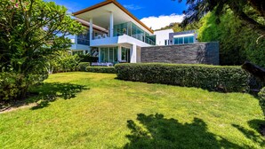 A modern two-story house with a large glass balcony, surrounded by well-maintained lawns and hedges.
