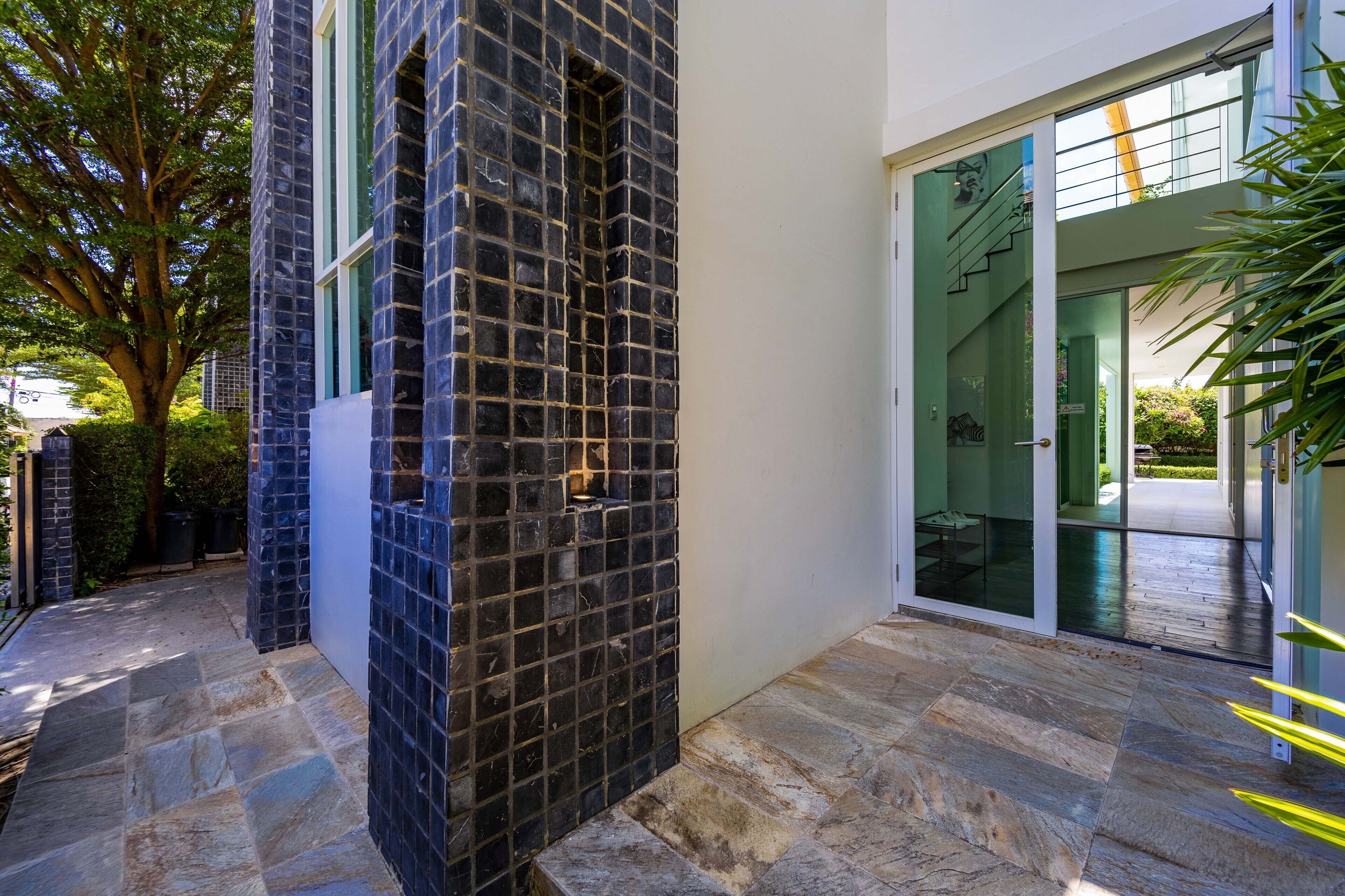 A modern building exterior with a stone-tiled entrance and a glass door leading to a covered outdoor area.