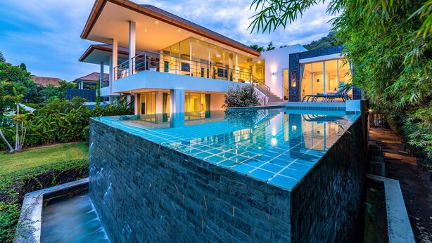 A modern two-story house with a glass-enclosed balcony, a swimming pool, and a well-maintained garden.