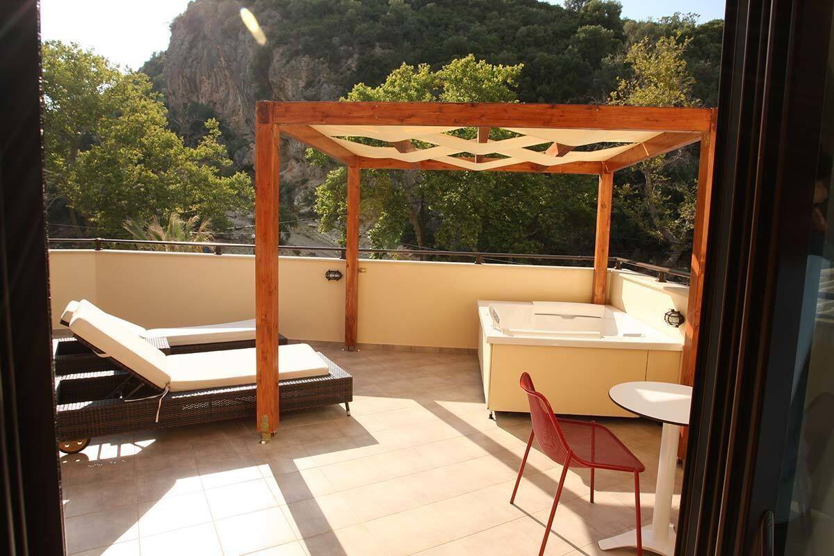 Un balcón con una pérgola de madera, una tumbona, una mesita y un jacuzzi.