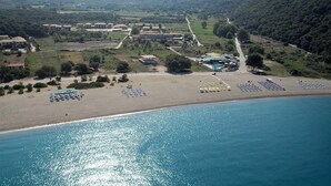 Ett flygbildsfoto av ett kustnära område med en strand, en swimmingpool och flera byggnader.