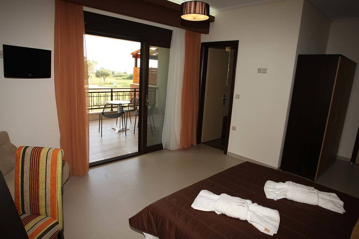 Habitación de hotel con cama, sofá, televisión y balcón con mesa y sillas.