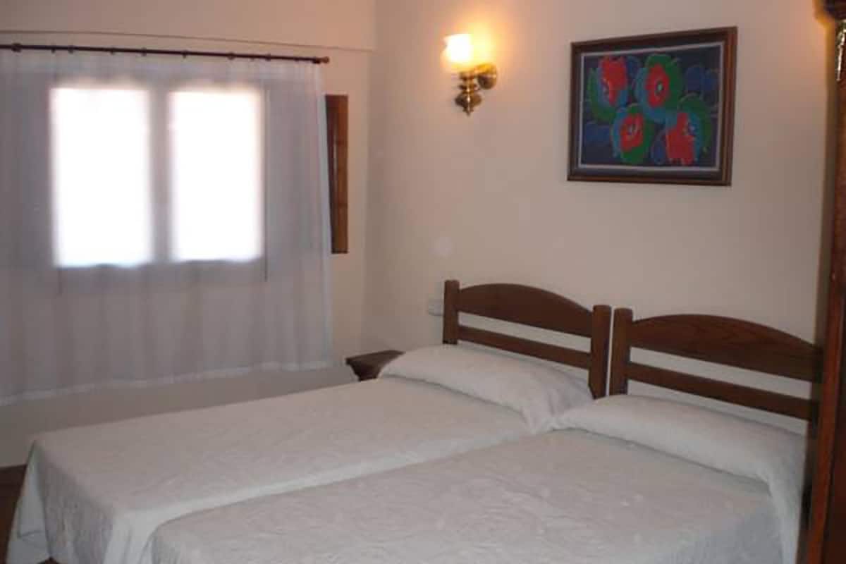 A room with two single beds, a nightstand, a wall-mounted light, and a window with a curtain.