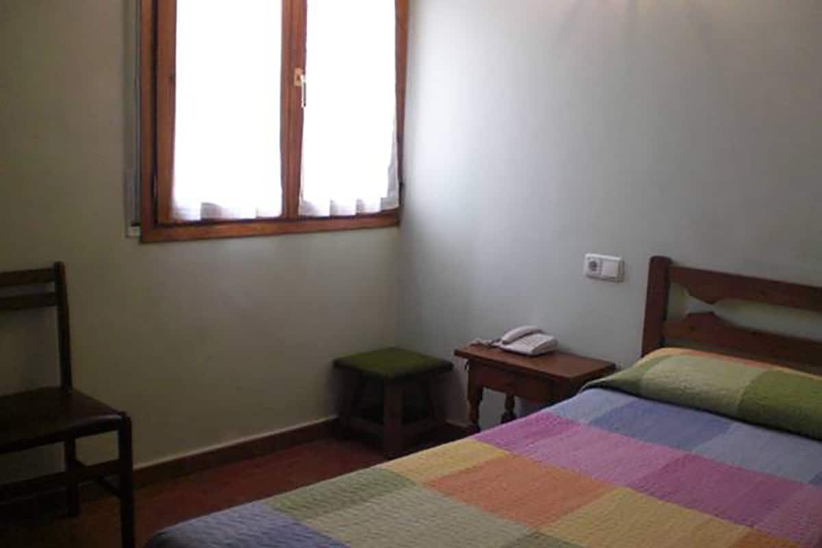 A bedroom with a bed, a chair, a nightstand, a small stool, and a window.