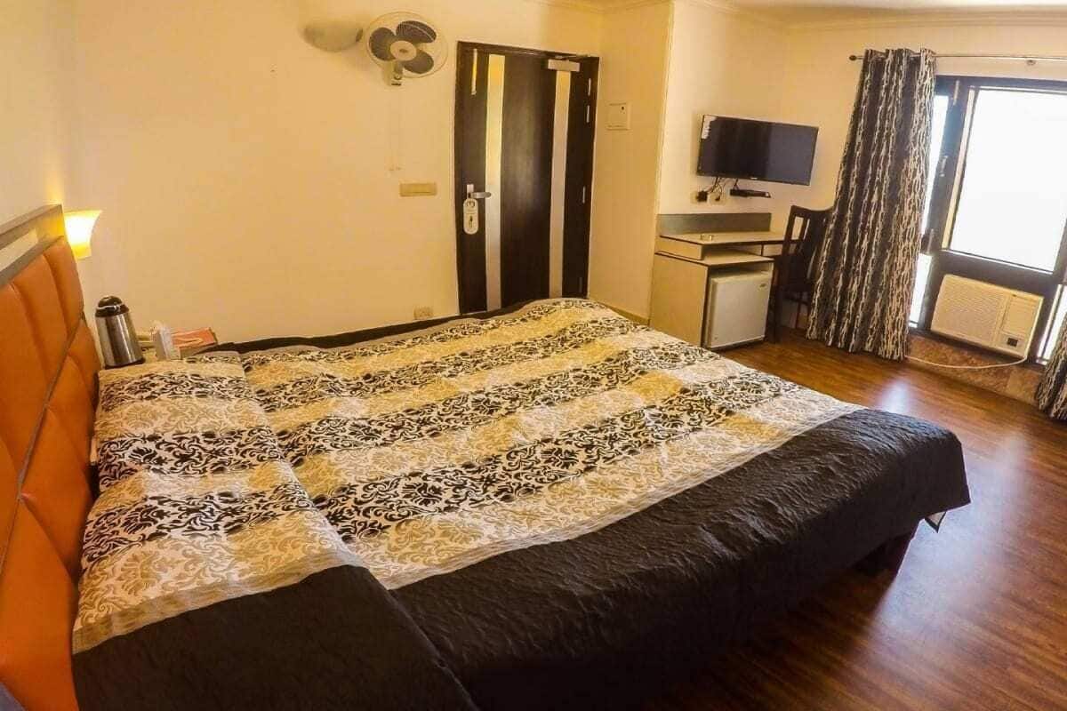 A hotel room with a bed, a desk, a television, and a window with curtains.