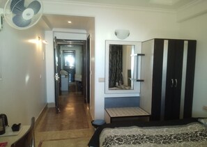 Une chambre d’hôtel comprenant un lit, une table de chevet, un miroir, une armoire et un ventilateur.