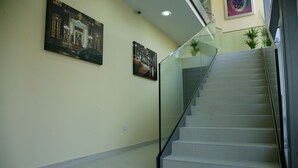 A staircase with glass railings leading to an upper floor, a plain wall with two framed pictures, and a tiled floor. - Hotel Contact (Belgrade)