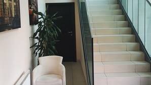 A modern lobby with a staircase, a seating area with a table, and a potted plant. - Hotel Contact (Belgrade)