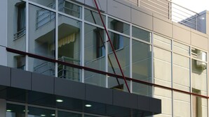 A modern building with a glass facade, a set of stairs leading to a door, and a small planter with two shrubs. - Hotel Contact (Belgrade)