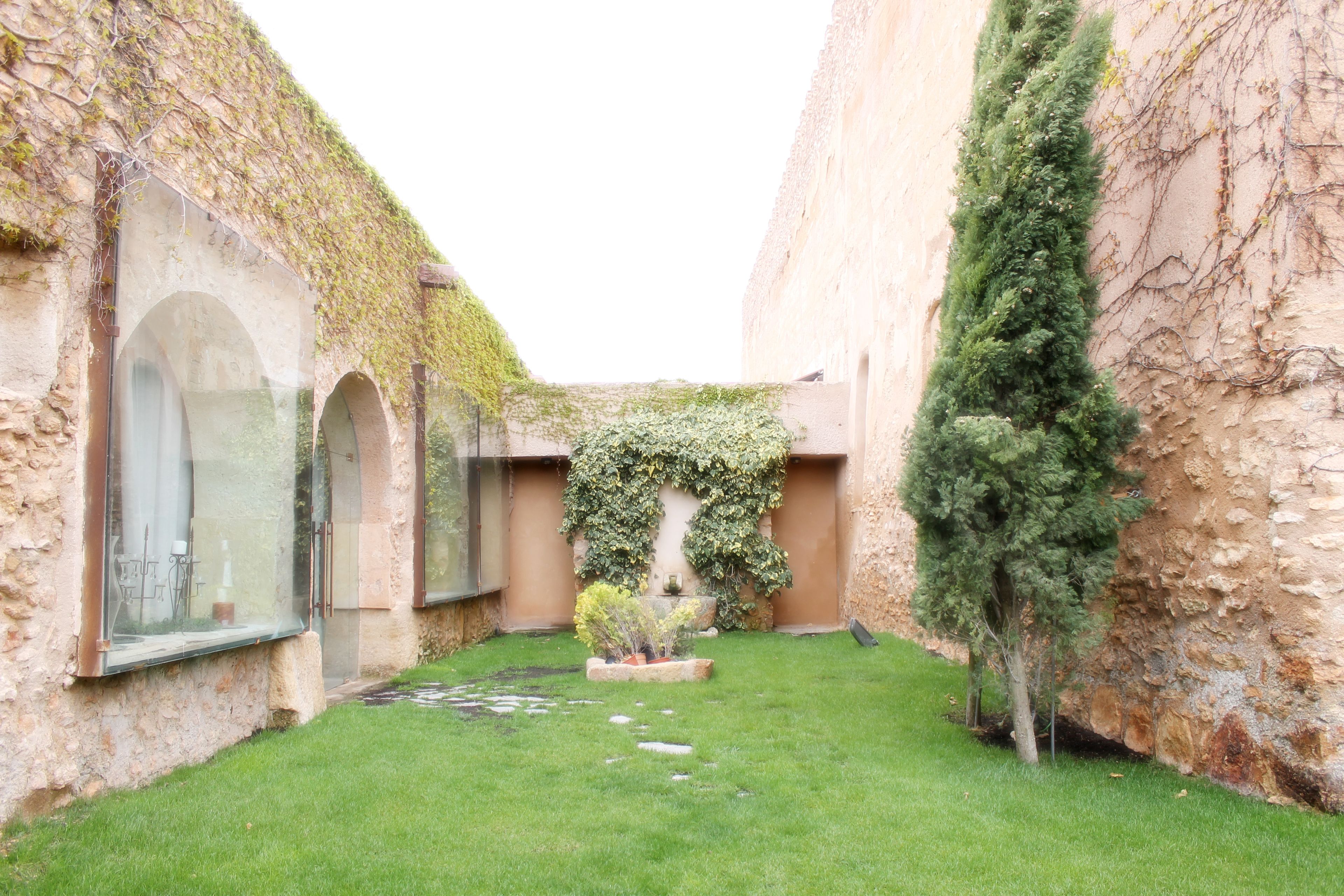 A courtyard with stone walls, a grassy area, and a small garden with plants and a fountain.