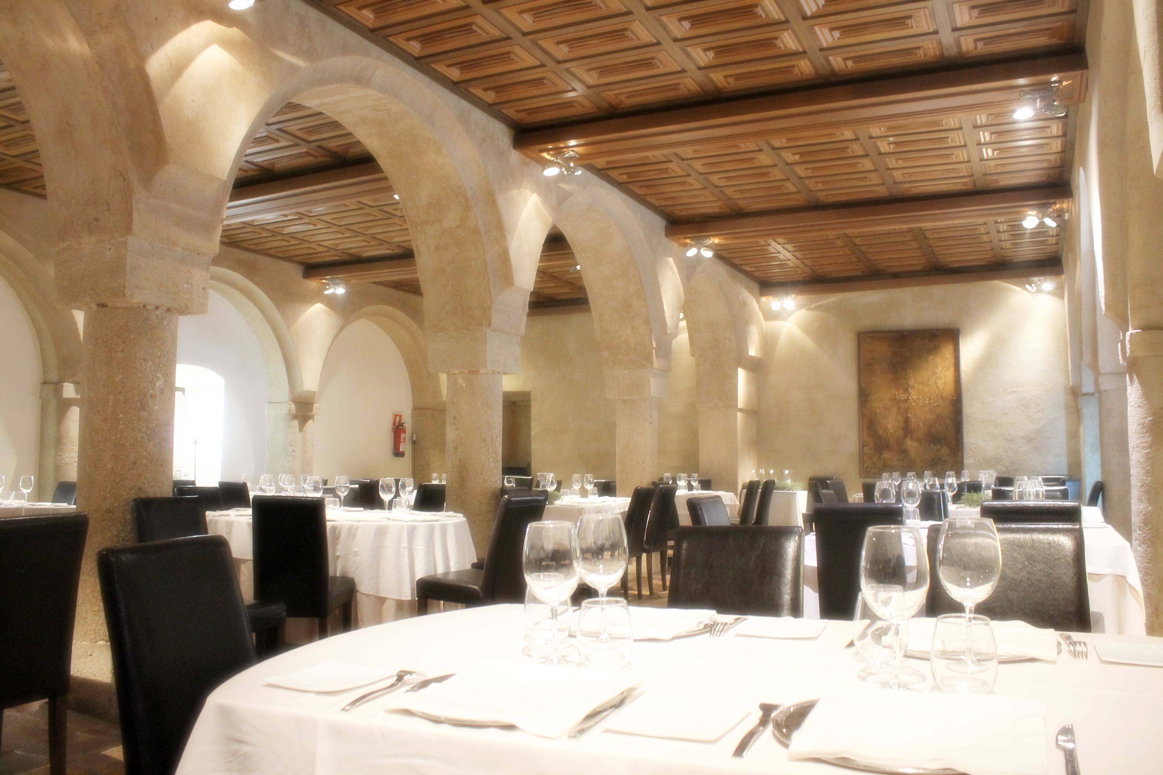 Un comedor con mesas redondas, manteles blancos y sillas negras.