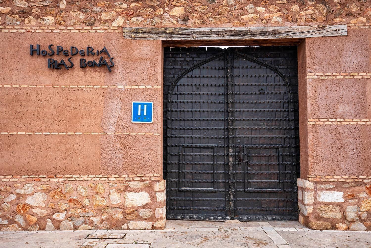 A stone building with a large black gate and a sign reading "Hospedaria Plas Banas".